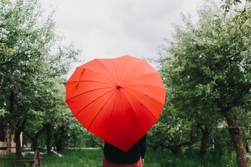 Pretty young woman hides behind heart shaped umbrella legs visible. Rain check