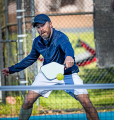 Male athlete volleys pickleball at the net