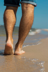 Beautiful young male legs walk along the beach. Warm summer weather