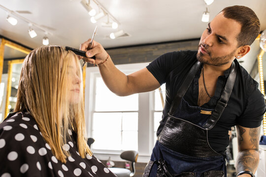 Stylist cutting young womans hair in polka dot cape at boutique salon 
