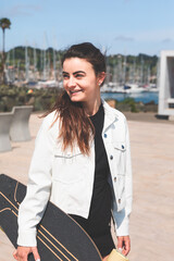 Young caucasian woman carrying a longboard at the sea side