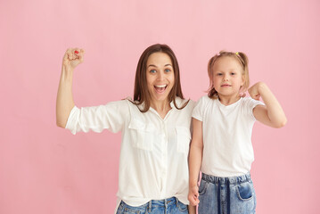 Mom and daughter show their muscles and strength in the studio on a pink background