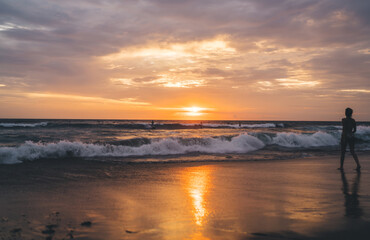 Unrecognizable person walking along ocean at sunset