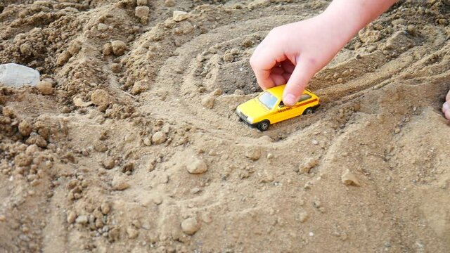A little boy plays with a small yellow car on the beach sand close-up