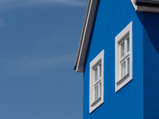 A section of a striking blue walled building with white windows against a blue sky.Contrasting colour in architecture