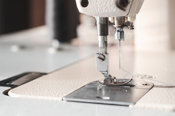 Industrial sewing machine needle steel presser foot with white thread for sew cloth close-up.