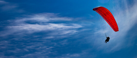 One paraglider flies on a red parachute in the blue sky. Paragliding on a sunny day. - obrazy, fototapety, plakaty