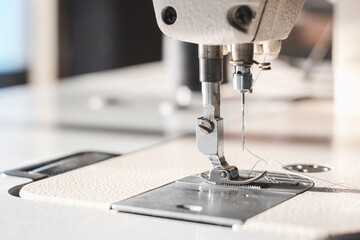 Industrial sewing machine needle steel presser foot with white thread for sew cloth close-up.