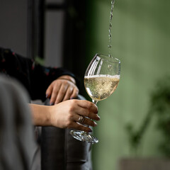 Female hands substitute wine glass under the pouring stream of white wine. Relaxing woman concept. Close up shot.