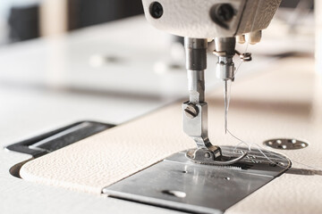 Industrial sewing machine needle steel presser foot with white thread for sew cloth close-up.