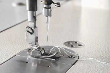 Industrial sewing machine needle steel presser foot with white thread for sew cloth close-up.