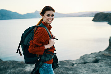 woman tourist at sunset near the sea in the mountains with a backpack on his back