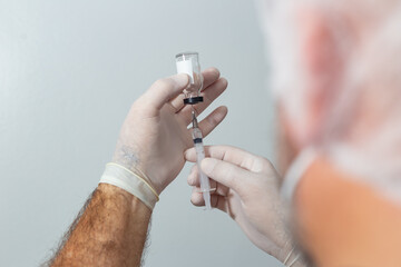 Detalhe de mãos com luvas de enfermeiro ou médico preparando a vacina para ser aplicada.