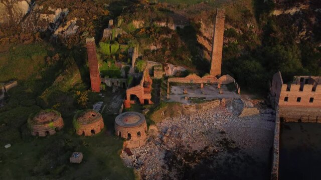 Porth Wen abandoned coastal derelict brickworks remains golden sunrise countryside bay aerial view birdseye orbit right