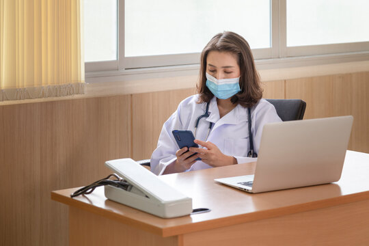 Asian Woman Doctor Sitting And Relaxing In Using Smartphone To Calls Family After Finished In Serious Patients Treatment In Covid Or Coronavirus Case In The Hospital.