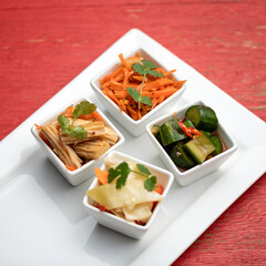 Set of oriental salads. Four kinds of spicy Thai vegetable snacks in white salad bowls. Spicy dishes of fresh and pickled vegetables with herbs on red tablewear. Healthy food. Soft focus.