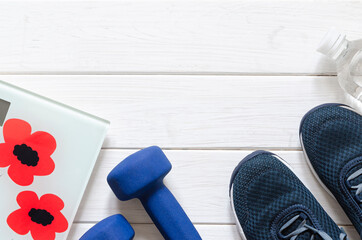Sport oufit on the white wooden background, top view, copy space. Blue sneakers, blue dumbbells and white scales flatlay