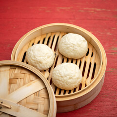 Chinese buns on bamboo steamer. Cooking pan-asian bread. Round pieces or balls of raw dough on wooden sieve or basket. Soft focus. Close up shot.