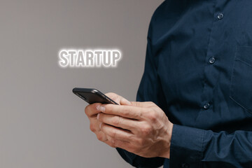 Close-up, the businessman's hands holding the phone and the Startup text. Concept of financing business, technology and people