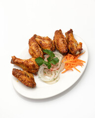 White platter with fried chicken wings with onions and parsley on white background. Roasted poultry meat on the bone. Food concept. Vertical format.