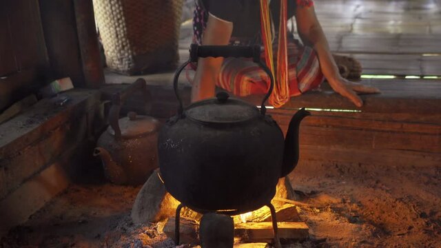 A portrait of karen tribe woman boiling water by using traditional kettle and fire, water heater at wooden kitchen at local home. People lifestyle.
