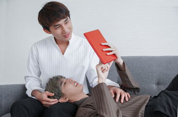 Close up of Asian young gay couple looking at tablet together on sofa at home. A man touch his...
