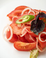 Close-up of fresh tomato salad with onion and basil on white plate. Healthy vegetarian food. Dietary vegetable meals with minimum of calories. Vitamin vital food. Soft focus.