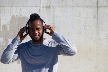 Obraz premium African-american man listening to music with white headphones. The man is happy because he likes music very much.