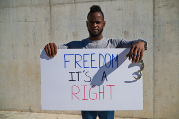 African-american man holds up a banner that reads freedom is a right. The man holds a shackle or handcuffs in his left hand. Human rights. Stop racism. Black lives matter.