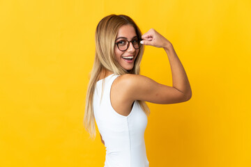 Young blonde woman isolated on yellow background doing strong gesture