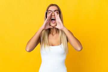 Young blonde woman isolated on yellow background shouting and announcing something