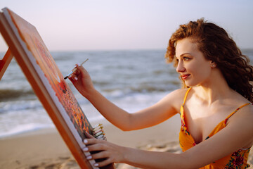Beautiful woman artist drawing her picture on canvas with oil colors at the beach. Art, creativity and inspiration concept.