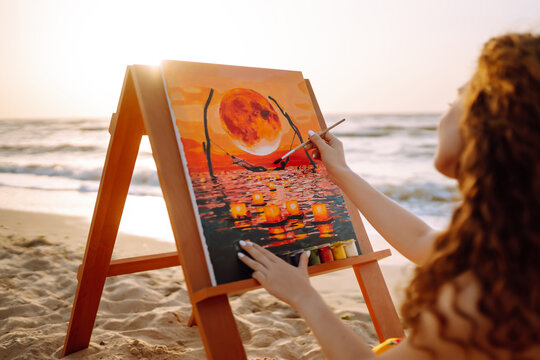 Beautiful woman artist drawing her picture on canvas with oil colors at the beach. Art, creativity and inspiration concept.