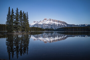 Rundle Mountain Range in Banff National Park with the reflection of the mountains and the trees in the lake 