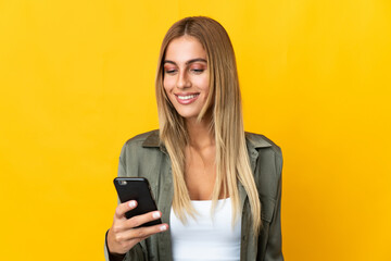 Young blonde woman isolated on yellow background sending a message or email with the mobile