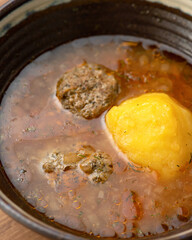 Bowl of hot rich broth. Close up shot. Fatty tomato soup with meatballs. Vertical format.