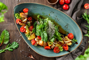 Baked potatoes with salad and tomatoes in plate on wooden background. Healthy vegan food, clean eating, dieting, top view