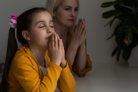 Religious Christian girl and her mother praying at home