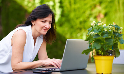 A woman types on her laptop while telecommuting outdoors