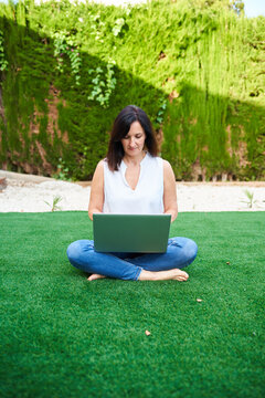 A brunette woman uses her laptop in the garden of her house