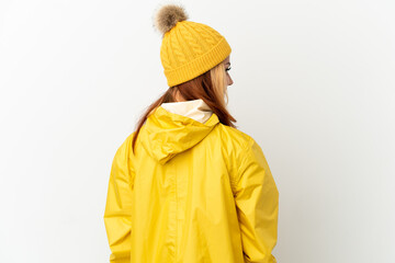 Teenager blonde girl wearing a rainproof coat over isolated white background in back position and...