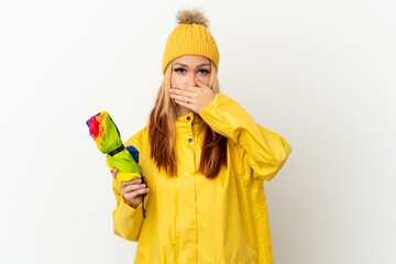 Teenager blonde girl wearing a rainproof coat over isolated white background covering mouth with hand