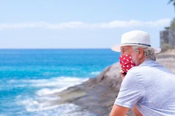 Coronavirus summer concept. Senior man wearing protective mask using mobile phone at sea vacation.  Horizon over the water