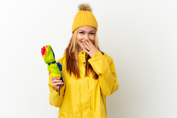 Teenager blonde girl wearing a rainproof coat over isolated white background happy and smiling covering mouth with hand
