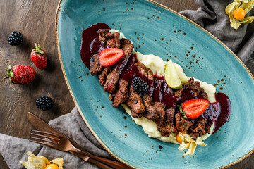 Baked meat with mashed potatoes and blackberry sauce in plate on wooden background. Healthy food,...