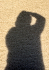 A strange posture of an unidentified person in shadow form against a tan colored grainy background.