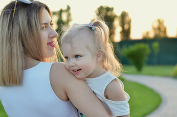 A small beautiful blonde blue eyed girl is sitting in her mother's arms and smiling