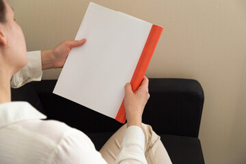 Beautiful female hands hold an open book or magazine in a room on a black sofa