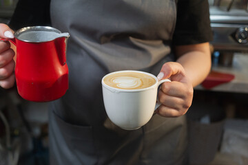 Woman bartender barista with a cup of cappuccino and milk in her hands in a cafe or coffee shop. The girl is holding coffee. Latte. Coffee making technology concept.
