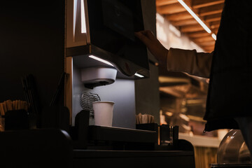 young woman prepares herself coffee through a self-service coffee machine in a cafe. woman near the...